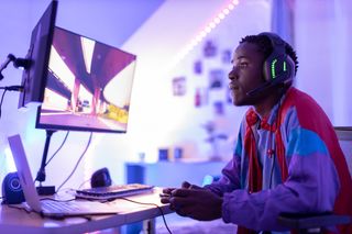 A man playing video games at a desk surrounded by a purple light.
