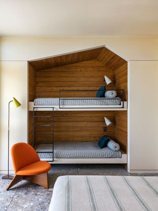 bunk beds build into a wall alcove, with an orange armchair next to the ladder and another bed visible at the front