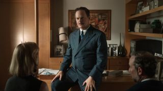 Press image of Rainn Wilson as Phil in Lessons in Chemistry leaning against his desk talking to Elizabeth and Walter.