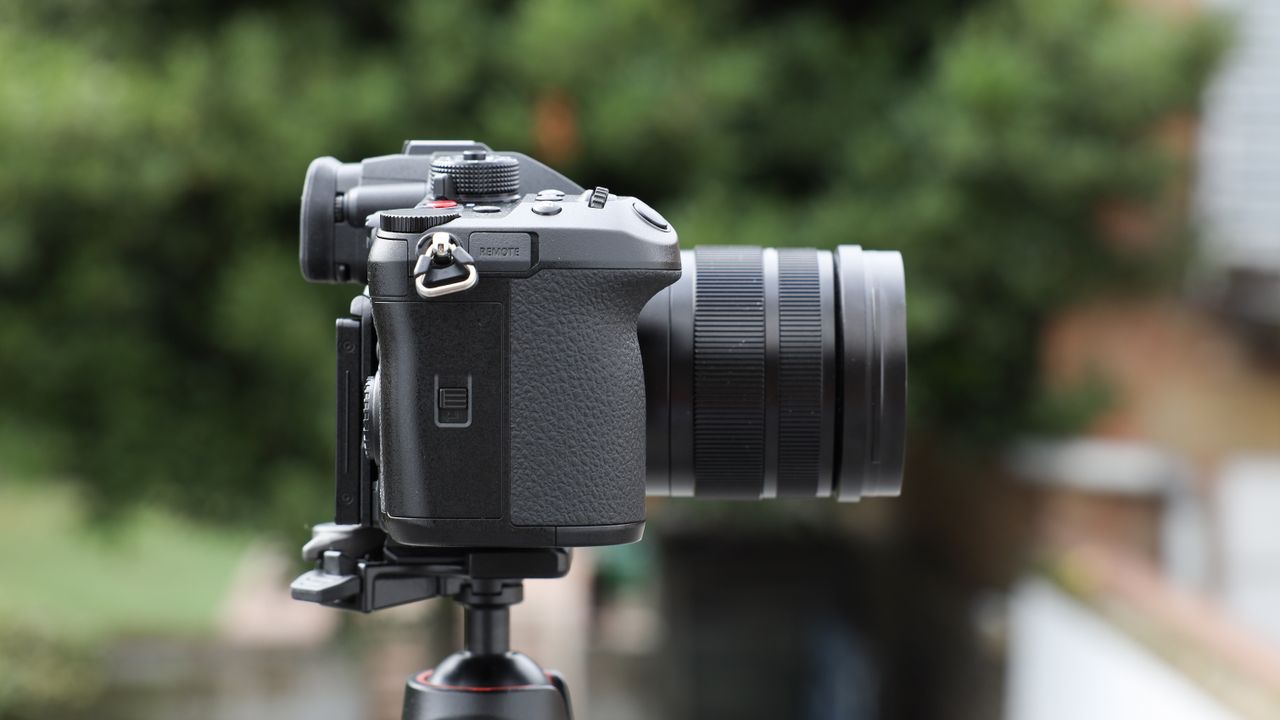 Panasonic Lumix GH7 on a tripod outside with some blurred green trees in the background