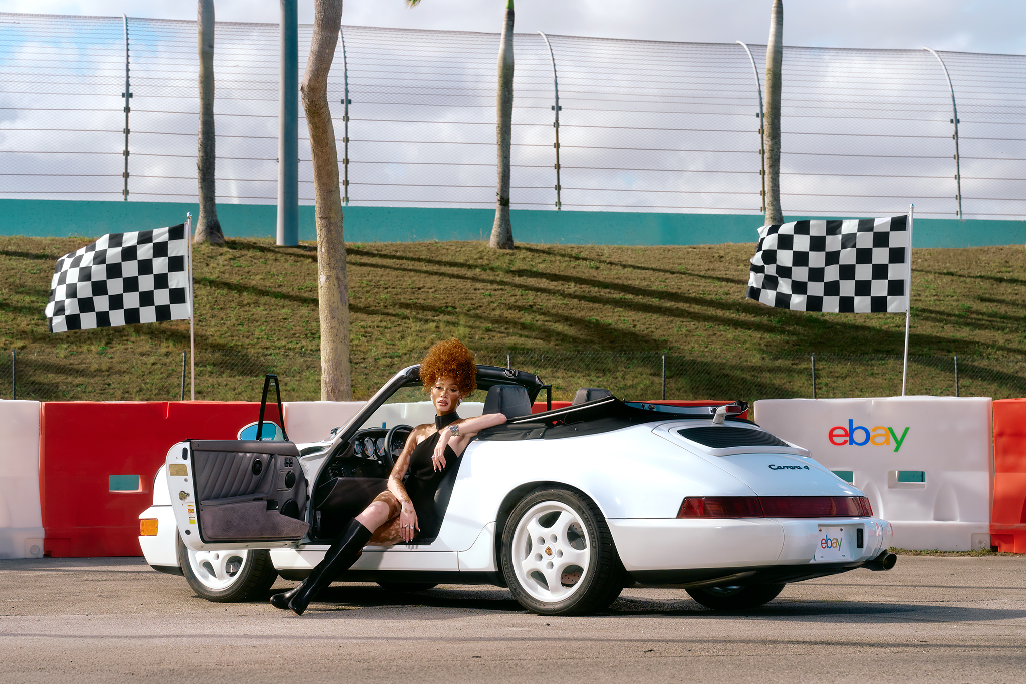 Winnie Harlow sitting in a car on the racetrack wearing knee high boots
