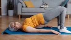 Woman in yellow T-shirt and grey leggings performing bridge exercise in domestic setting