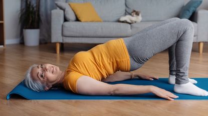 Woman in yellow T-shirt and grey leggings performing bridge exercise in domestic setting