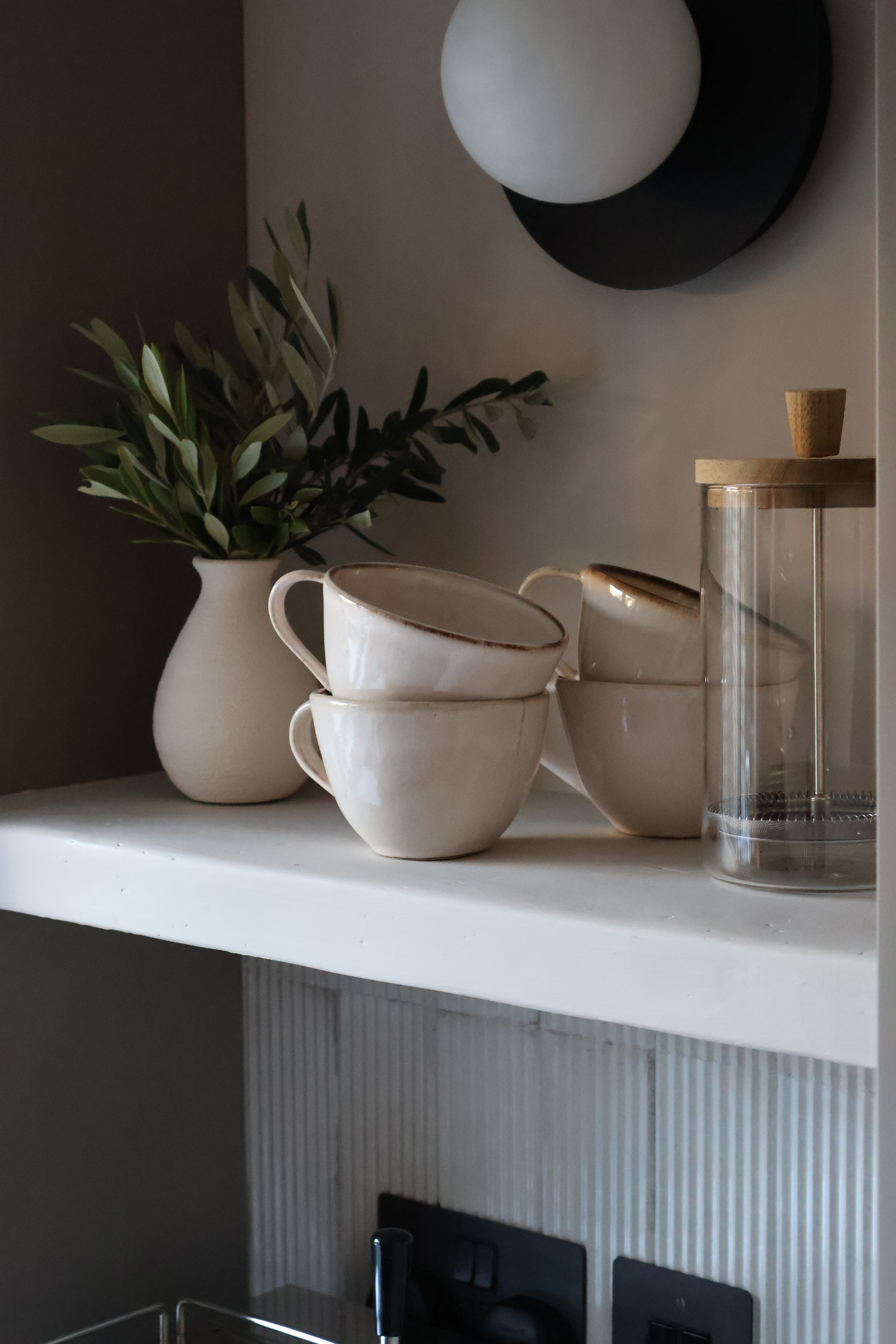 coffee mugs on a plastered shelf with a vase of olive branches