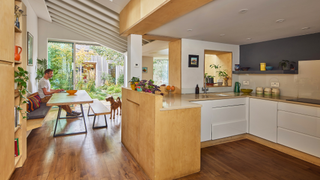 Open plan kitchen diner with wooden floor, beamed ceiling, and view into the garden from the patio doors 