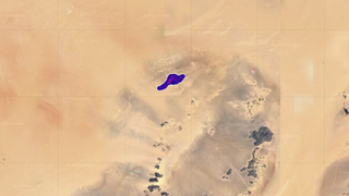 An aerial view of a sandy-colored area. A dark purple splotch represents the methane plume source EMIT detected.