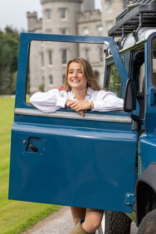 Tati Reed poses outside a Scottish Castle in the door of her Land Rover Defender