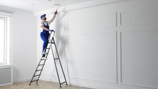A man standing on a ladder painting the ceiling with a roller