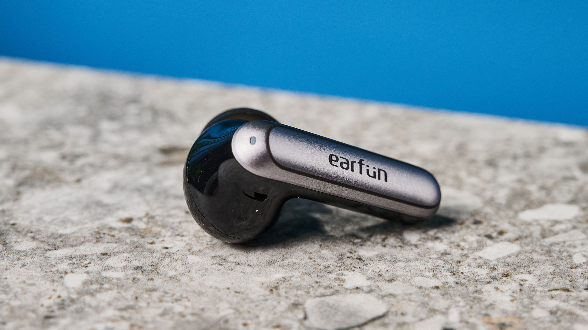 a pair of black and silver earbuds with silicone tips and a black charging case are photographed against a blue background