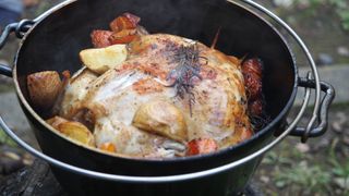 A whole chicken cooking in a camping dutch oven