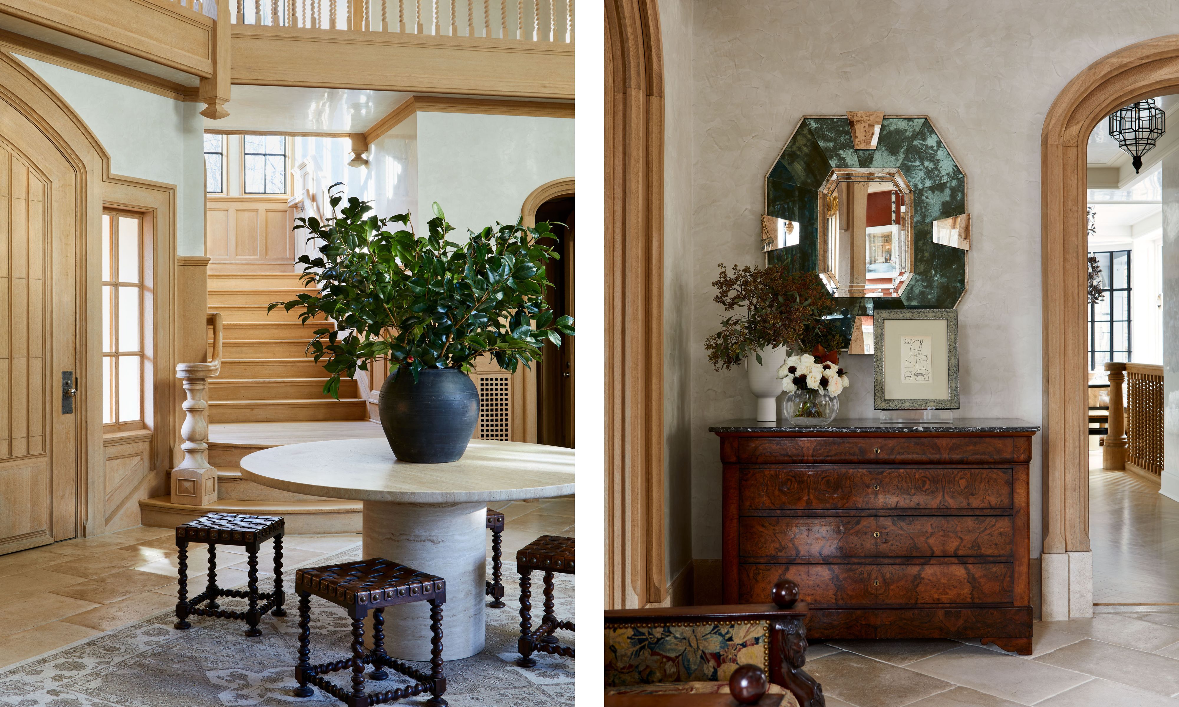 A large entrance hall with a wooden staircase, exposed woodwork, cream plaster walls, and a large stone circular table. A corner of an entryway with an arched doorway, an antique dresser, and an antique green mirror above it.