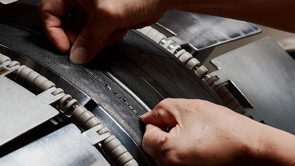 A close up of a pair of hands attaching an &#039;American Classic&#039; logo to a tyre in production