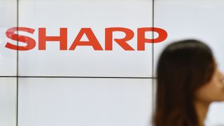 Sharp logo pictured at a Tokyo train station with woman walking past in foreground.