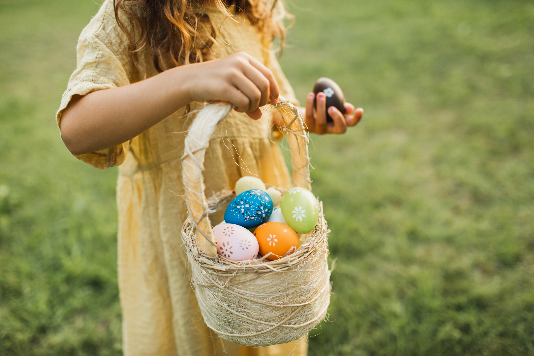A child wearing a yellow dress, holding an Easter basket full of colourful Easter eggs.
