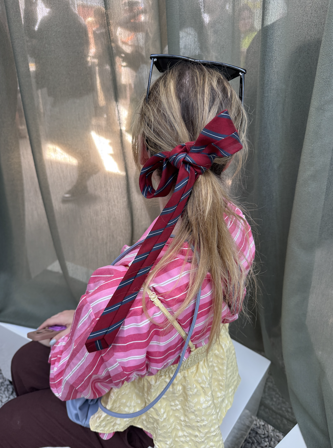 a guest at Copenhagen Fashion Week wears a tie in her hair with a striped shirt