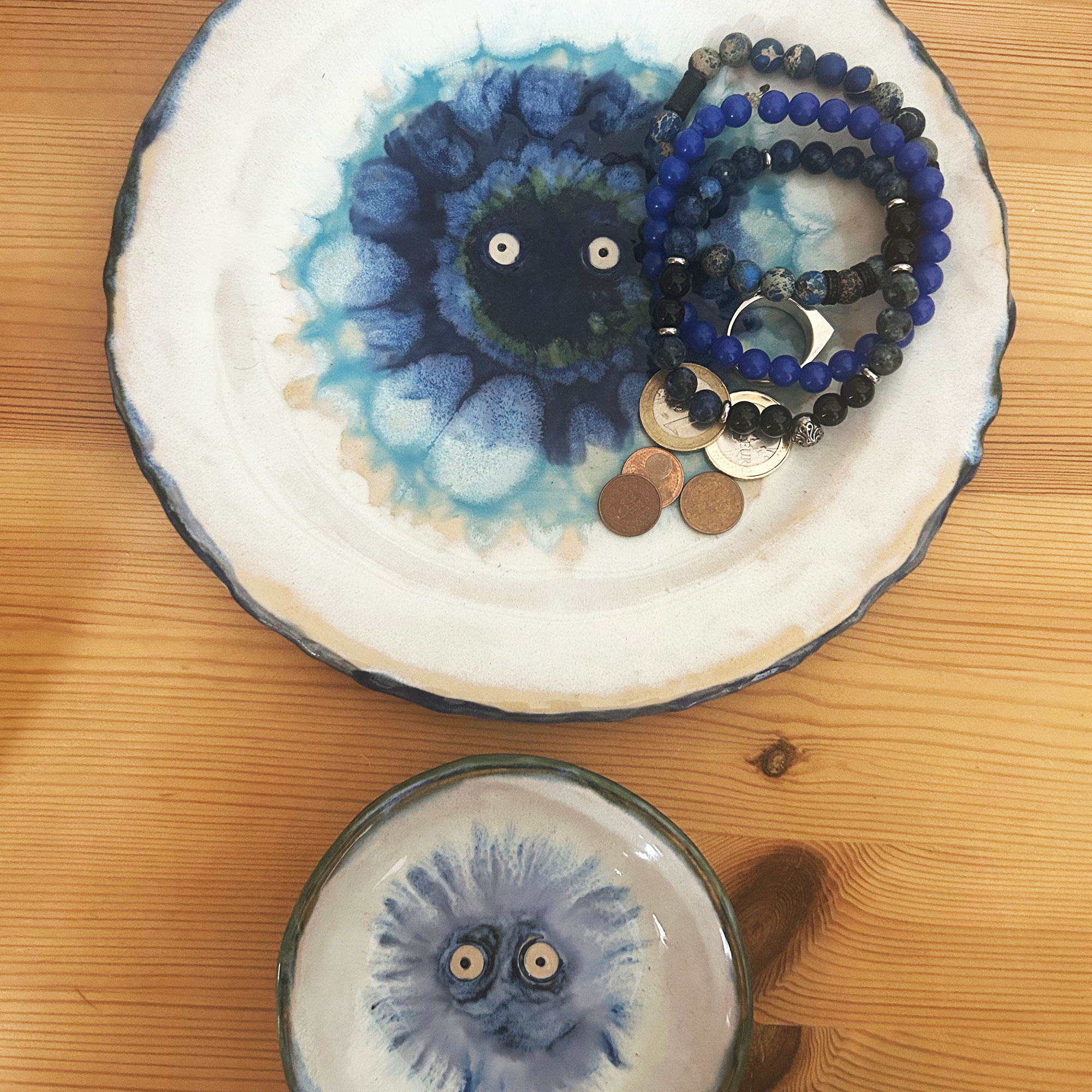 Two dishes with blue glazing and set of eyes in centre, with bracelets and loose change resting on the larger of the two