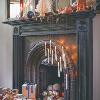 A Christmas-decorated black fireplace with floating candle lights and Christmas baubles coming out of it