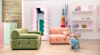 Green sofa and peach chaise in a white walled room with squiggly-surround full length mirror and white floating shelves with bag and shoes on