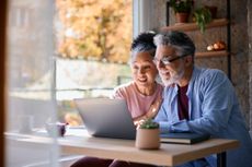 Surprised senior couple sitting together at home, gazing at their laptop screen, sharing in the joy of good news and experiencing a moment of happiness and connection