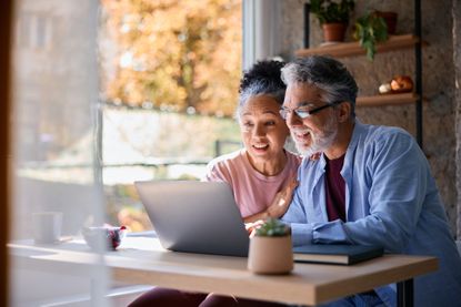 Surprised senior couple sitting together at home, gazing at their laptop screen, sharing in the joy of good news and experiencing a moment of happiness and connection
