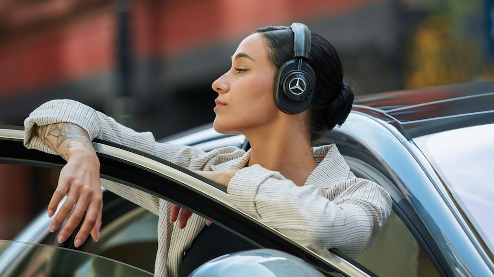 Master &amp; Dynamic MW65 Mercedes-Benz headphones worn by a woman, standing in the doorway of a car