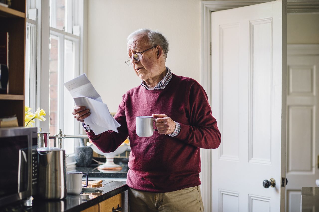 Senior man standing in the kitchen of his home with a letter