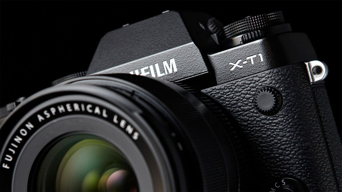 Close-up of black Fujifilm X-T1 on a black background, with Fujinon lens obscuring the Fujifilm logo, but providing a close-up view of the X-T1 logo 