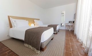 Ecorkhotel bedroom with two beds with white linen and brown throw at footends of beds