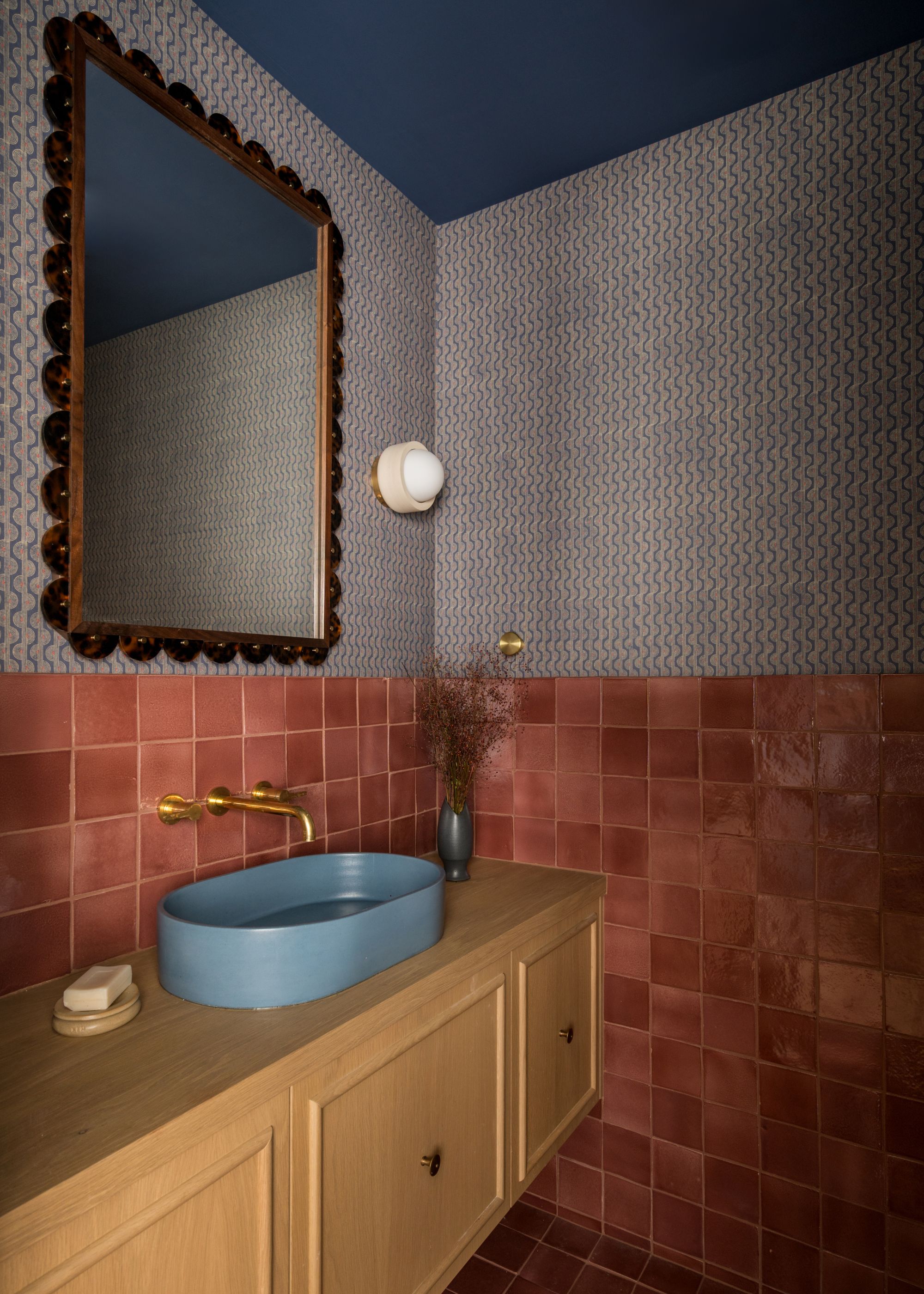 A bathroom with red tiling and blue speckled wallpaper with blue painted ceilings and a blue sink