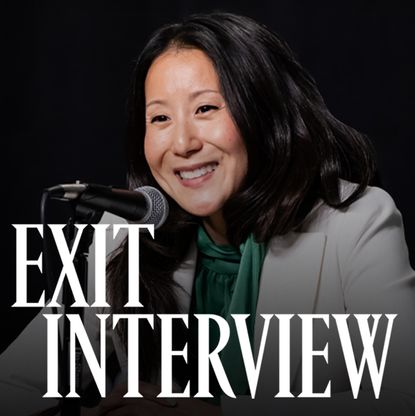 A photo of USA Gymnastics president and CEO Li Li Leung smiling in front of a microphone against a black backdrop.