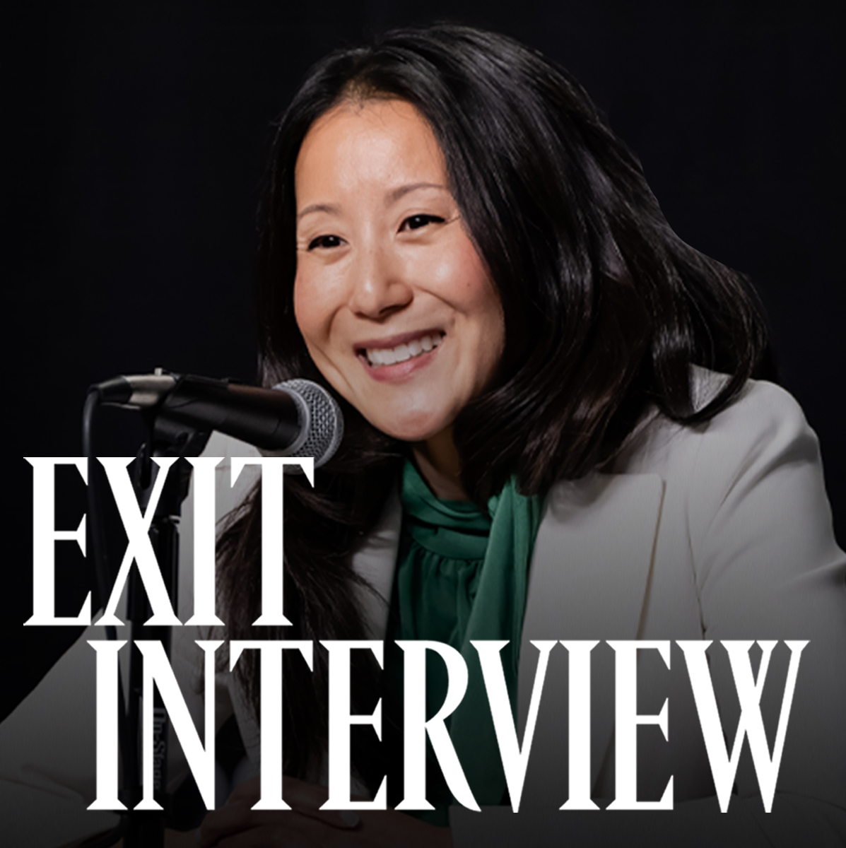 A photo of USA Gymnastics president and CEO Li Li Leung smiling in front of a microphone against a black backdrop.