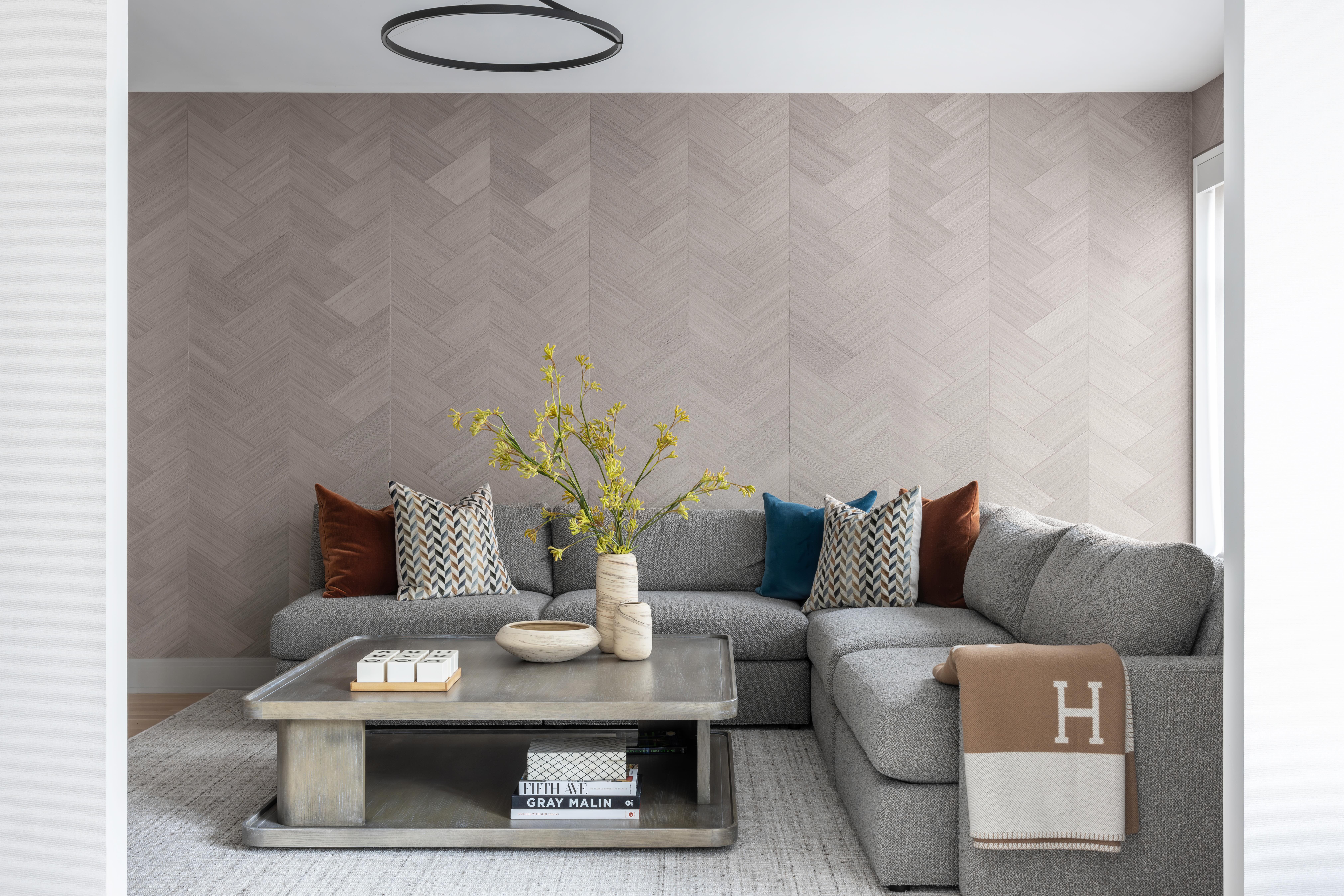 A modern living room with a gray sectional sofa and brown and white and blue pillows.