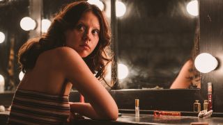 Mia Goth looking over her shoulder in front of a makeup mirror in X.