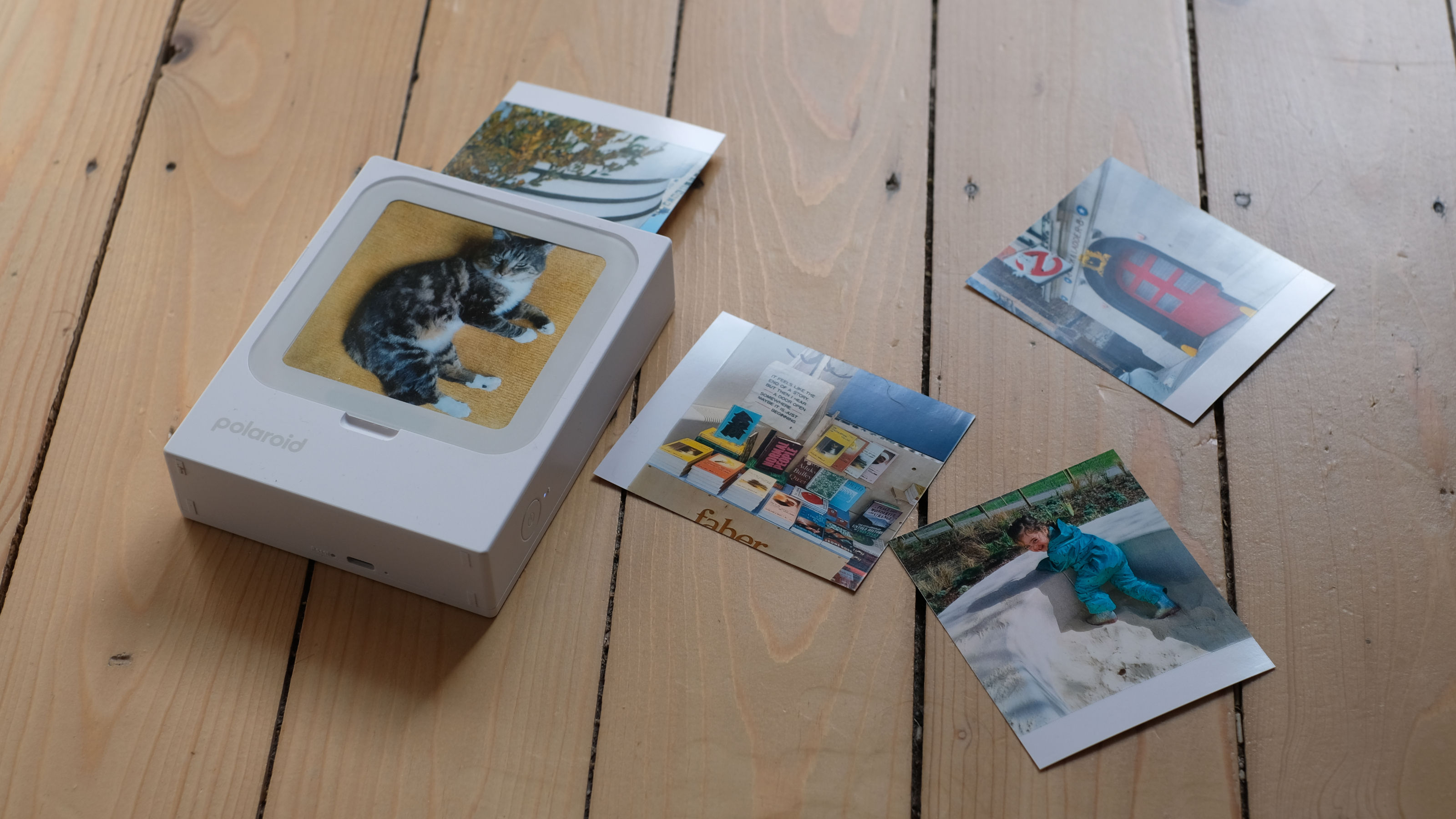 Photograph of Polaroid Hi-Print 3x3 mini instant printer mid-print, with prints on the floor beside it.