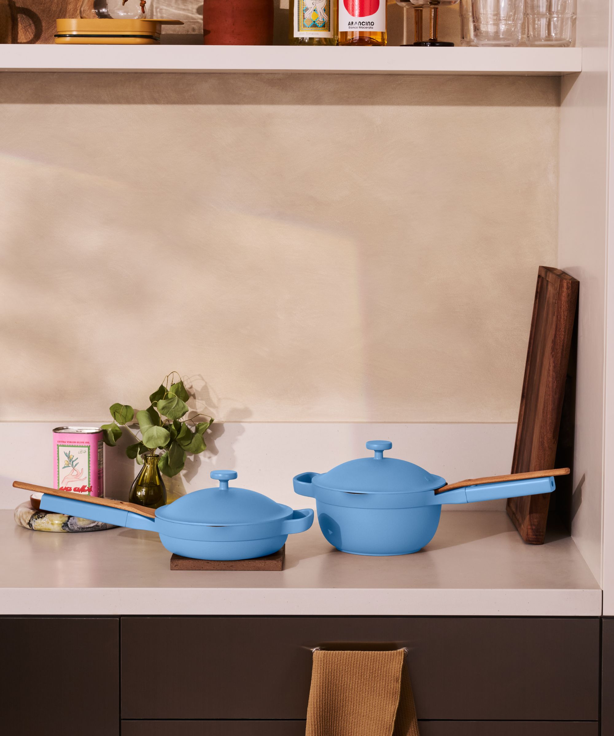 Two blue pans (a frying pan, and a deeper pot with a long handle) sit beside one another on a white kitchen countertop. They both had matching domed shaped lids on top.
