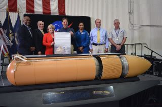 NASA and California Science Center officials present a signed title transfer document for the last space shuttle external tank, ET-94, during a ceremony at the Michoud Assembly Facility on Tuesday, April 12, 2016. Pictured from left to right: Bobby Watkins, Michoud Assembly Facility director; Parker Counts, NASA’s project manager for the external tank from 1992-1999; Jody Singer, Marshall Space Flight Center deputy director; Jeffrey Rudolph, California Science Center president; Jeanette Epps, NASA astronaut; Steve Cash, former space shuttle propulsion office manager; and Dennis Jenkins, project director for Endeavour's display at the California Science Center.