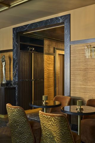 an art deco style hotel dining room with patterned seats, wall covering, a marble trim around the doorway and glass fluted pendant lights