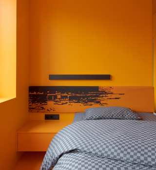 A bright orange wall and a grey bed