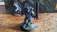 A Space Wolf model holding a gun and chainsword on a wooden table