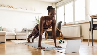 Woman doing press up at home in front of workout laptop