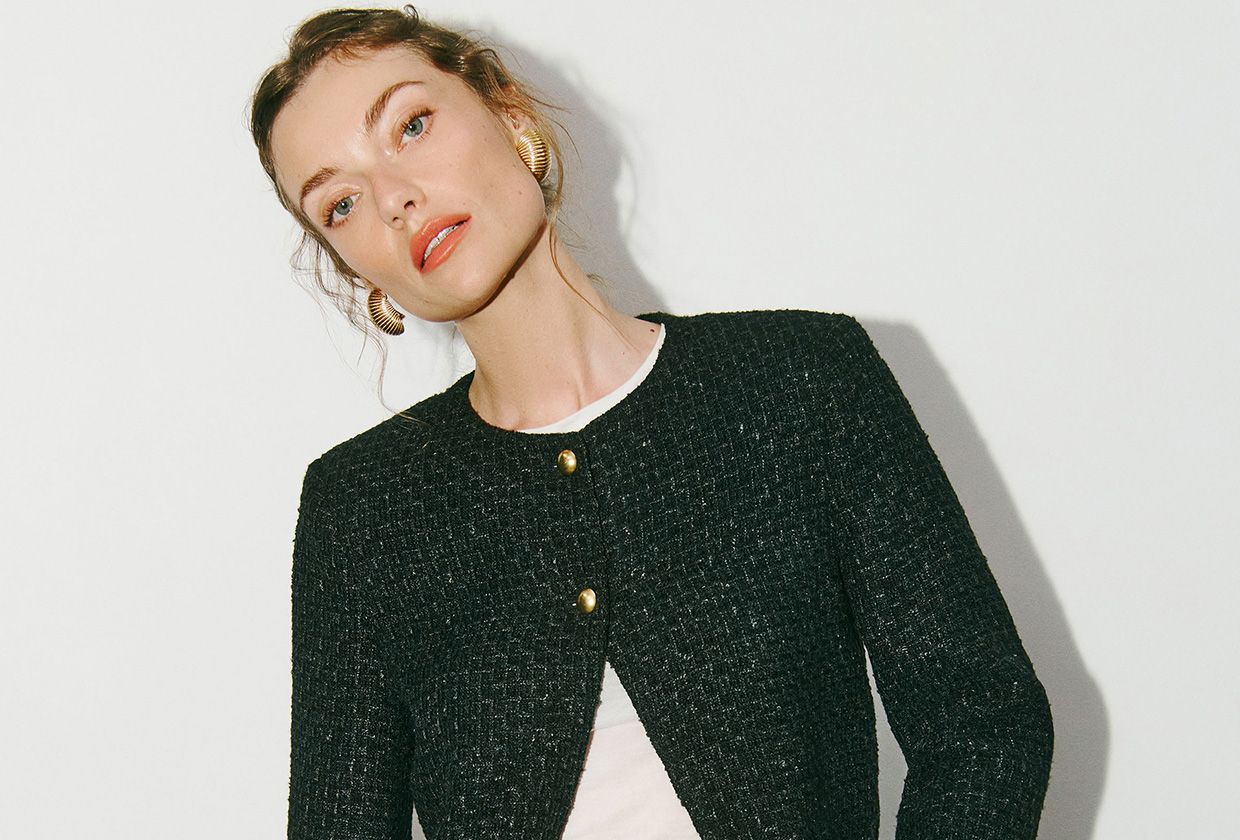 Reformation model wearing a black tweed jacket with a white, cropped tee and short black shorts.