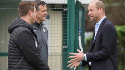 Prince William talking to two men while wearing a suit 