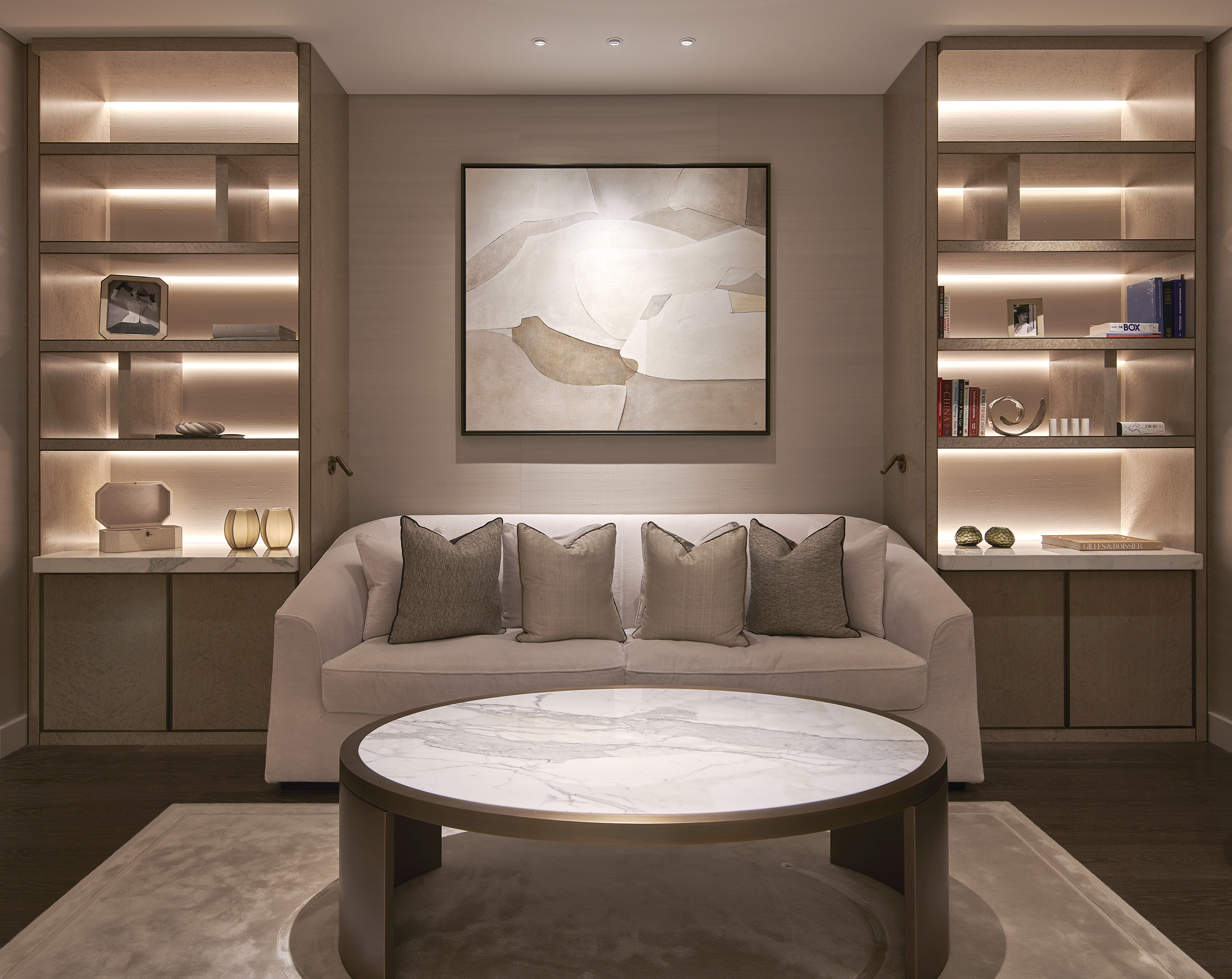 Neutral colored living room featuring a rug, coffee table, sofa, central wall art, and LED backlit shelves showcasing decorative objects.