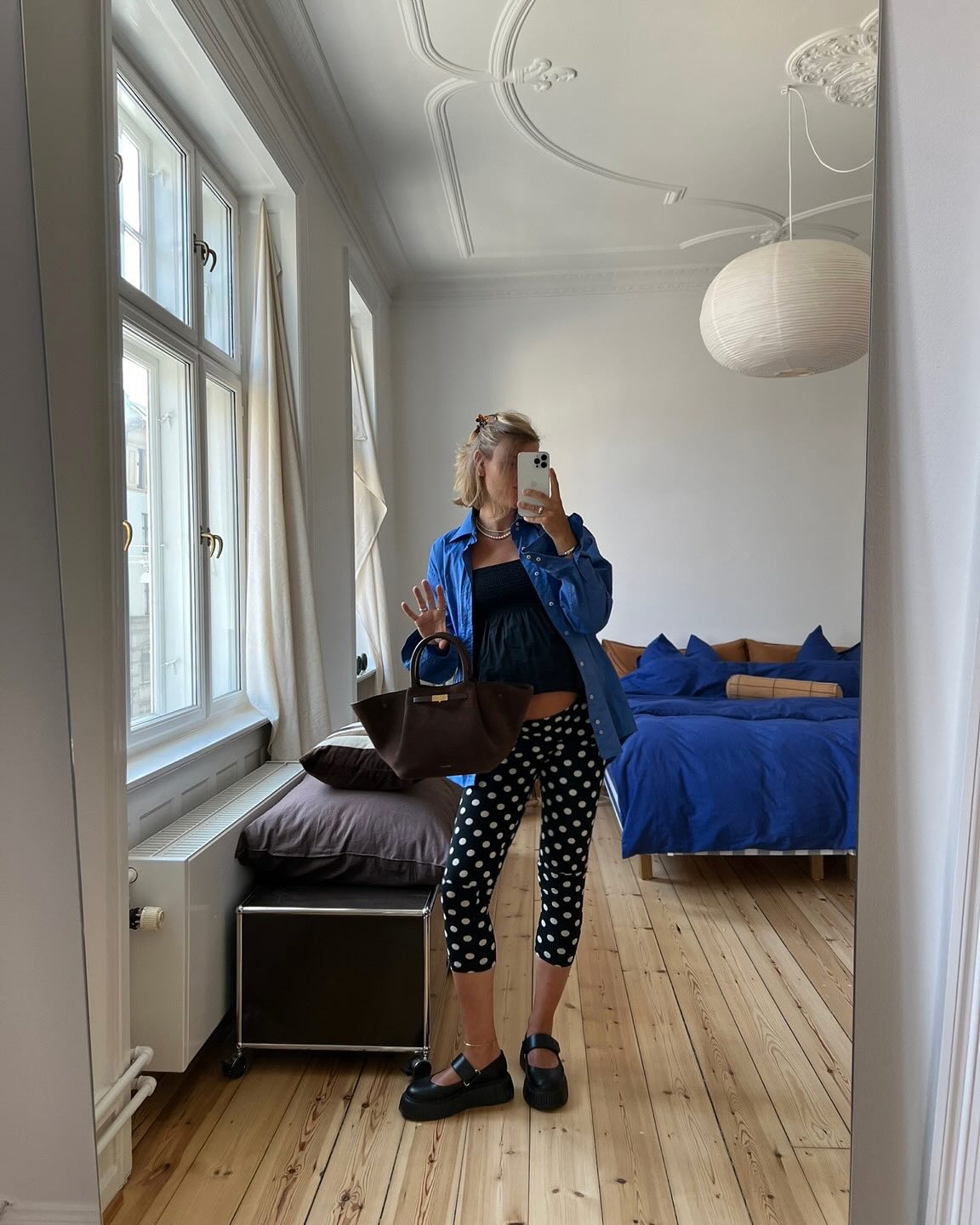 Influencer @amalienielsenn takes a mirror selfie wearing black capri pants with white polka dots, platform mary janes, a brown suede handbag and a cobalt blue shirt.