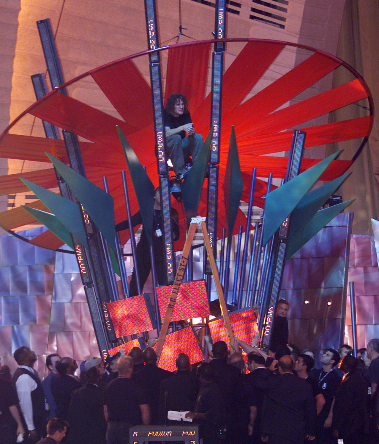 Tim Commerford halfway up the MTV VMAs set in 2000, surrounded by a group of men