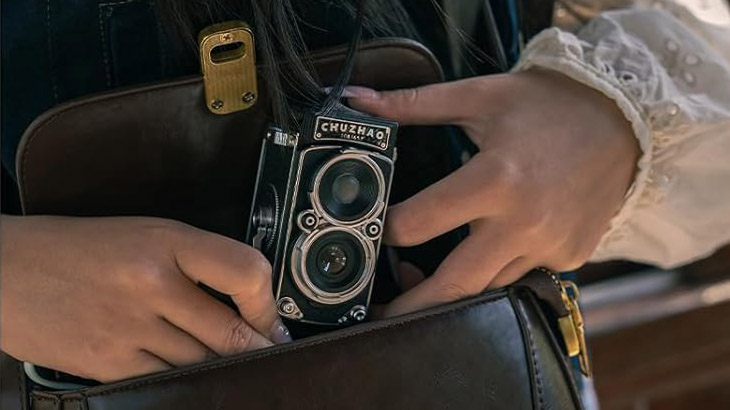 A lifestyle product picture of the CHUZHAO Retro TLR 12MP Digital Camera being pulled out of a dark brown shoulder bag