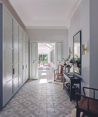 Hallway with grey and white tiled floor and built in cupboards on the left and console table and chairs to the right, view through to kitchen and garden.