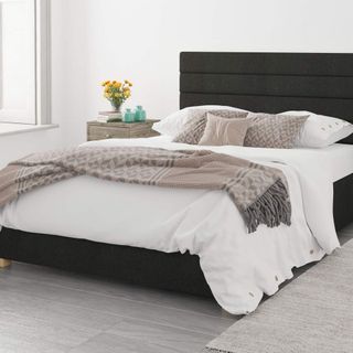 A dark grey storage bed with white bedding