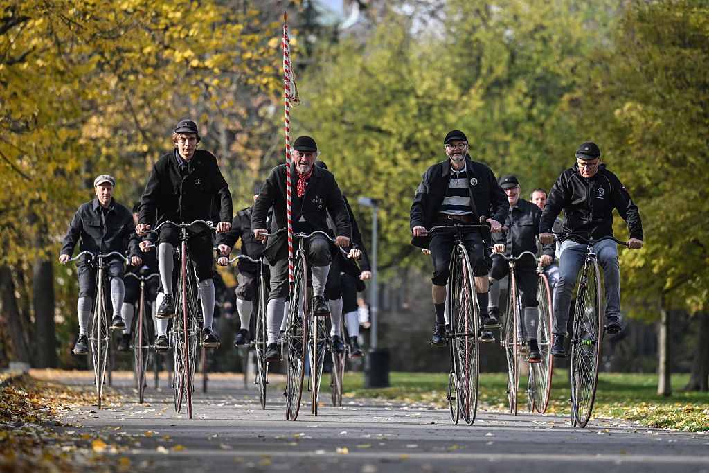 men riding penny farthings with big wheels in a park