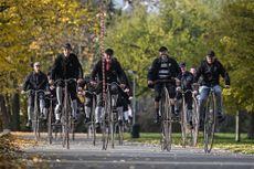 men riding penny farthings with big wheels in a park